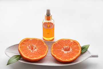 Two halves of cut tangerine on a white wooden plate and a bottle of aromatic essential tangerine oil on a white background.