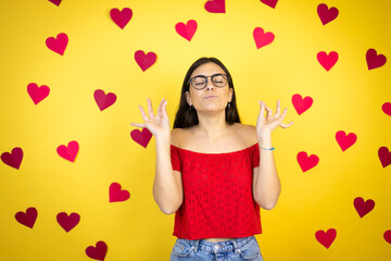 Obraz na płótnie Canvas Young beautiful woman over yellow background with red hearts relax and smiling with eyes closed doing meditation gesture with fingers