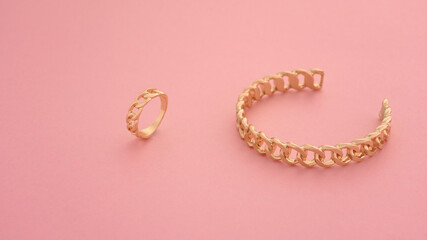 Top view of chain shape golden bracelet and ring on pink background
