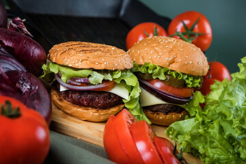 A delicious burger next to a fluted frying pan. A chef's knife. Lots of vegetables.