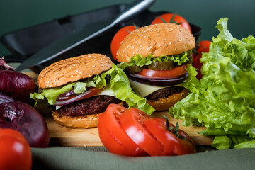 A delicious burger next to a fluted skillet. A chef's knife. Lots of vegetables.