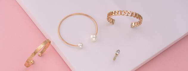 Panoramic shot of golden bracelets and ring on white and pink paper