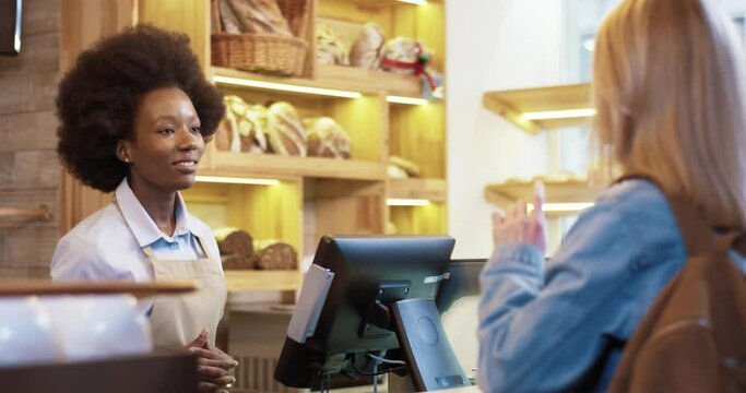 Beautiful african american saleswoman in baket shop serves client carefully listening order and advising on availability of goods.