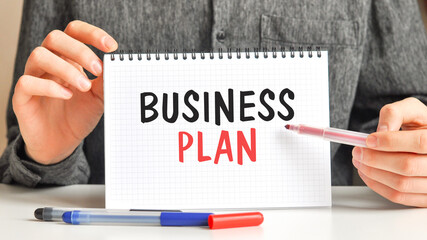 A sheet of paper with text BUSINESS PLAN, multicolored markers on a white table. Business and educational concept.