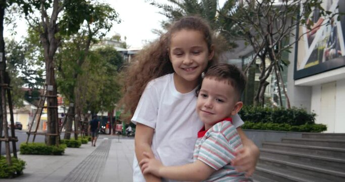Children, a little curly girl sister are hugging her brother. Little brother and sister hug and kiss in front of the camera. Family, two children on the street doing pose for the camera.