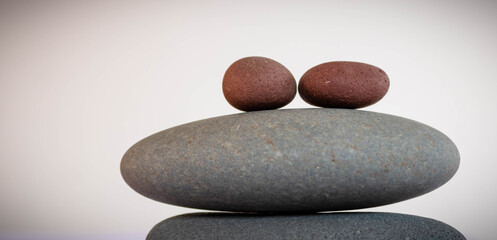 Two red round pebbles  on top of two oval grey  pebbles on a white background, concept of simplicity
