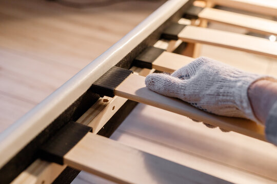 Male worker's hand in glove assembling bed, connecting slats to bed frame
