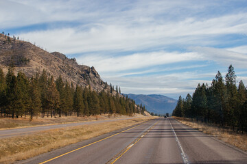 Fototapeta premium Beautiful autumn landscape on a bright sunny day, which depicts a highway, high mountains ahead and a clear blue sky with fluffy gray-white clouds