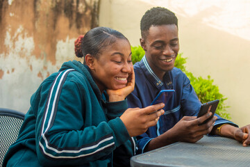 young black man and lady happy together with their smart phones while sitting outdoor.