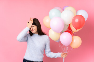 Young Ukrainian teenager girl holding lots of balloons over isolated pink background having doubts with confuse face expression