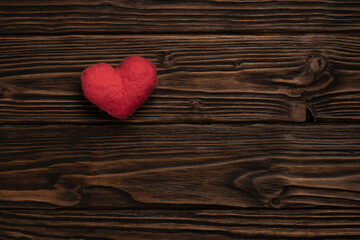 Red woolen handmade heart on the dark brown textured wooden boards