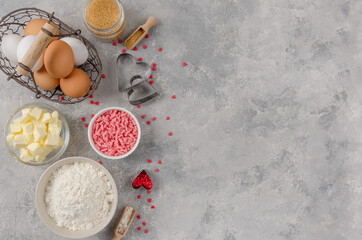 Ingredients for cooking cookies for Valentine's Day, flour, butter, eggs, sugar, chocolate and sugar hearts on a gray concrete background. Valentine's Day background. Copy space.