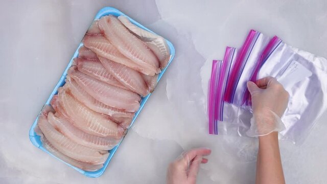 Tilapia fillet in plastic container and zip lock bags close up on marble background, copy space, flat lay