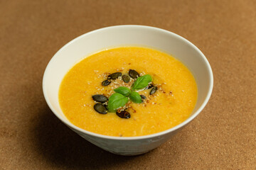 pumpkin cream soup with basil and pumpkin seeds served in a white ceramic bowl