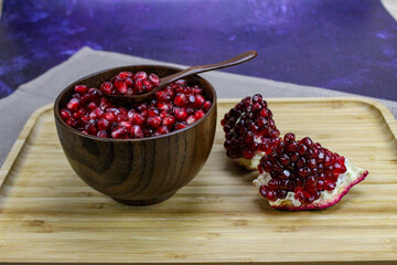 Red pomegranate seeds close up in a wooden bowl with a wooden spoon. Two pieces of pomegranate with ripe red seeds on a wooden tray.