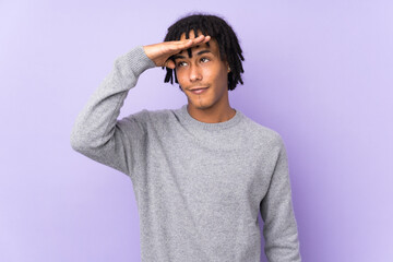 Fototapeta na wymiar Young african american man isolated on purple background looking far away with hand to look something