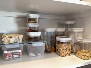 An organized pantry shelf with various types of cookies, cereal and snacks  and snacks