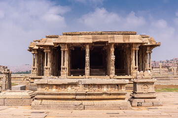 Obraz premium Hampi, Karnataka, India - November 5, 2013: Vijaya Vitthala Temple. Beige stone ruinous sacntuary manadapam with sculpted pillars under blue cloudscape.