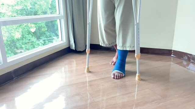 A male patient in splint walking with crutches in hospital, step forward walk with crutches for injured leg or leg splint. healthcare concept
