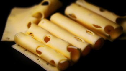 Rolls of cheese on a black background. Cheese with holes rolled into a tube.