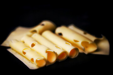Rolls of cheese on a black background. Cheese with holes rolled into a tube.