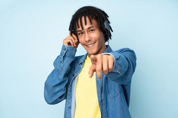 Young african american man isolated on blue background listening music and pointing to the front