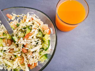 salad.  Fresh salad with cucumber, cabbage and tomatoes on a table. Fresh orange juice 