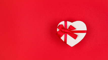 White heart shape gift box with red ribbon on red background with copy space, banner, top view....