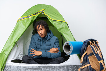 Young african american man inside a camping green tent making doubts gesture while lifting the shoulders