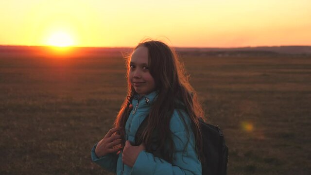A girl traveler walks with a backpack on her back and smiles at the sunset in the sky. A teenager on a camping trip on vacation. Childhood in search of adventure from morning to dawn. Love for the