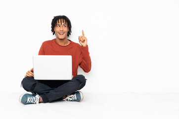 Young african american man sitting on the floor and working with his laptop intending to realizes the solution while lifting a finger up