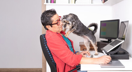 Latino freelancer working on his computer with external monitor and graphic tablet while his dog is crossed