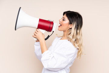 Teenager girl isolated on beige background shouting through a megaphone