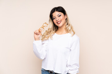 Teenager girl isolated on beige background with glasses and smiling