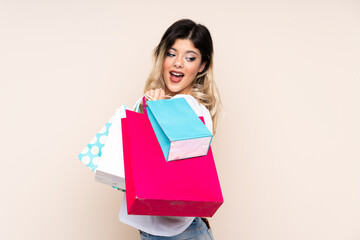 Teenager girl isolated on beige background holding shopping bags and looking back