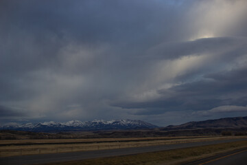 Autumn landscape at dusk. Asphalt road among steppes with yellow dry grass, blue mountains on the horizon, beautiful blue-gray autumn sky. Montana, USA, 11-23-2019