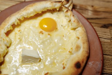 Top view on traditional Adjarian Khachapuri - open baked pie with melted salt cheese suluguni and egg yolk on wooden tray. Traditional georgian food