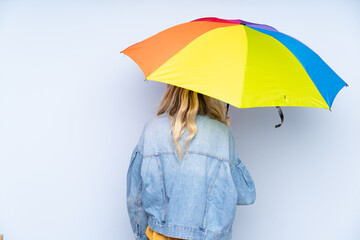 Teenager russian girl holding an umbrella isolated on blue background in back position