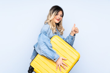 Traveler teenager holding a suitcase isolated on blue background in vacation with travel suitcase...