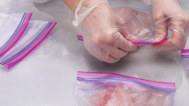 Fresh raw fish fillet in zip lock bags. Tilapia fillet on light marble background, close up. Woman hands put  fillet in zip lock bags for freezing