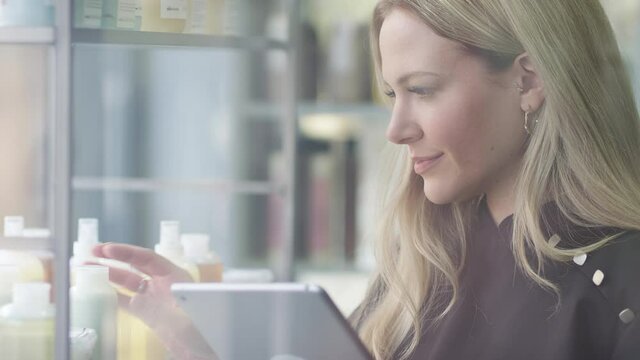 Female Business Owner In Hairdressing Salon With Digital Tablet Checking Beauty Products 