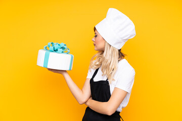 Teenager girl pastry holding a big cake isolated on yellow background looking side