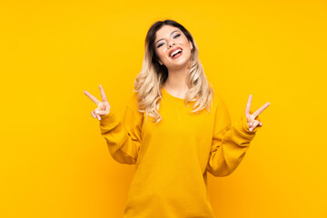 Teenager girl isolated on yellow background smiling and showing victory sign