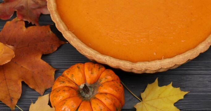Tasty pumpkin pie and autumn leaves on wooden table, closeup