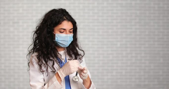 Doctor taking off protective goggles, rubber gloves and medical mask against light background