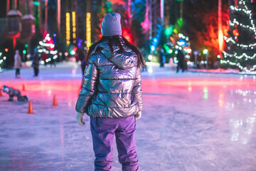 Girl ice skating on the ice rink arena with happy people in the background, concept of ice skating in winter, winter activities, holiday christmas time, with new year decoration and illumination