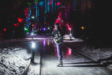 Girl ice skating on the ice rink arena with happy people in the background, concept of ice skating in winter, winter activities, holiday christmas time, with new year decoration and illumination