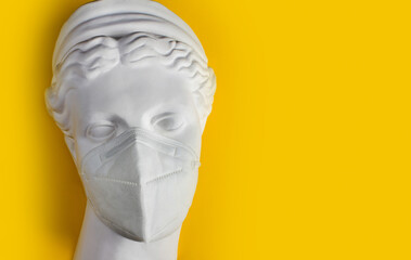 Photo of a female greek gypsum statue face with medical protective mask on it on yellow background.