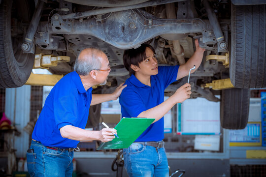 Engineer car mechanics pose checking under car by see detail document on hand to maintenance and fixed car in garage.