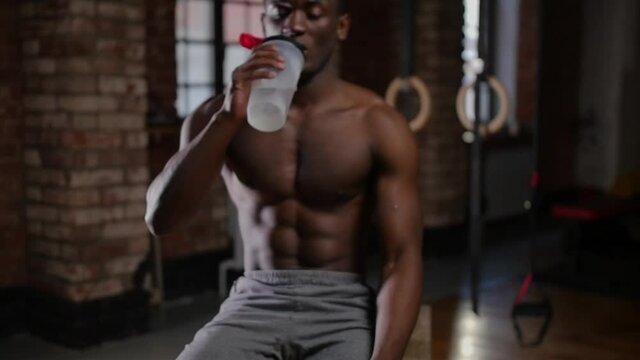 A shirtless african-american handsome man training in the gym - drinking water from the plastic bottle